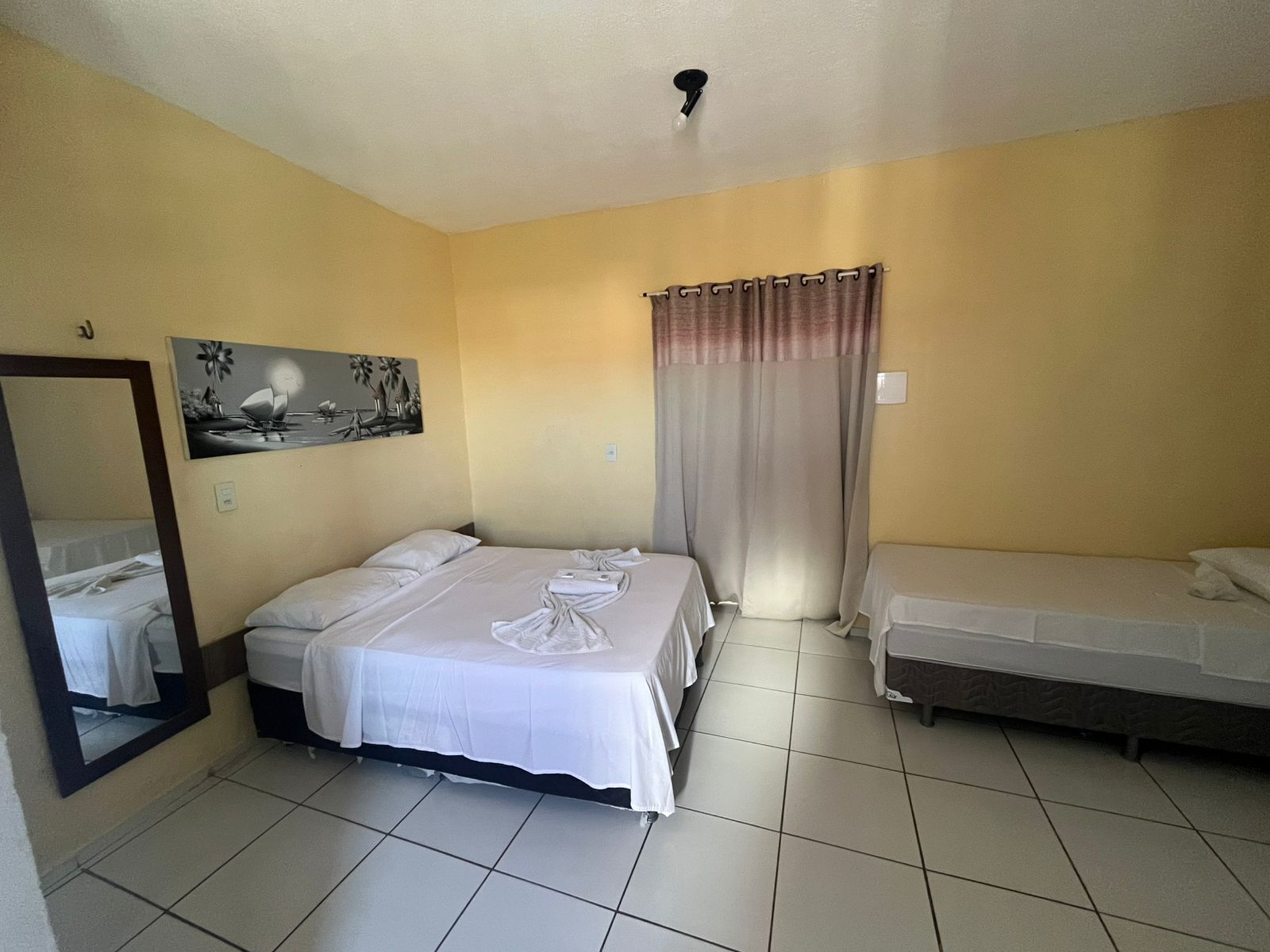A hotel room with two beds, a large mirror, a painting, and a curtain.