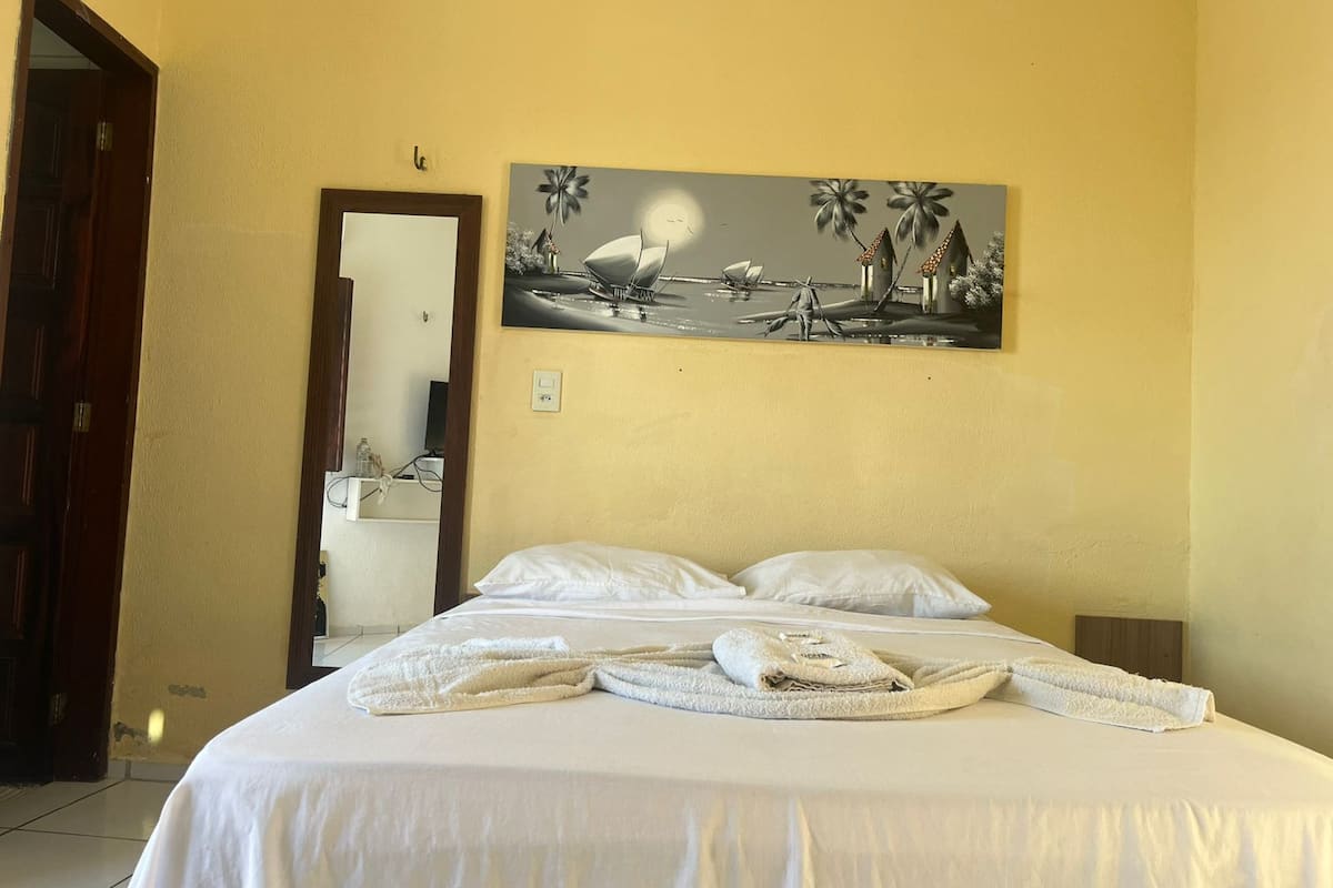 A hotel room with a bed, white linens, a painting of a beach scene, and a door to the left.