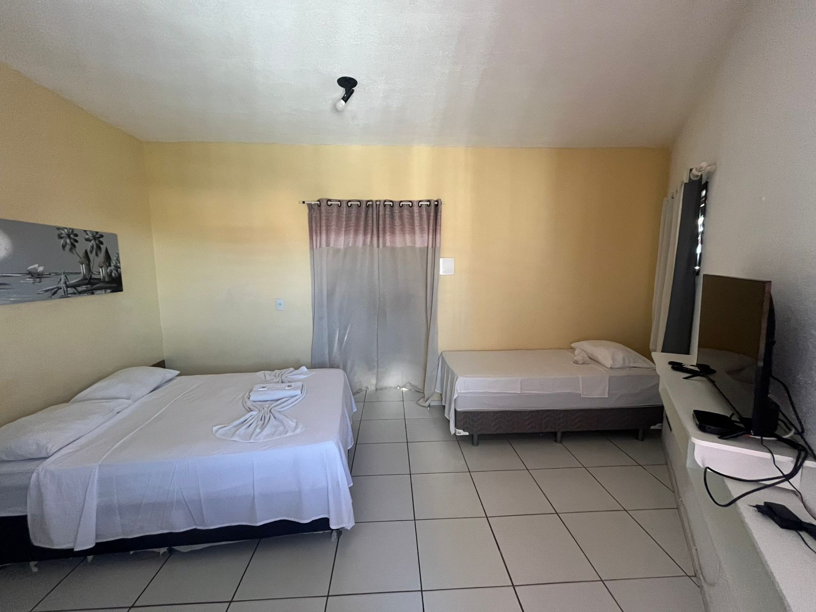 A hotel room with two single beds, a small desk with a chair, a television, and a curtain.