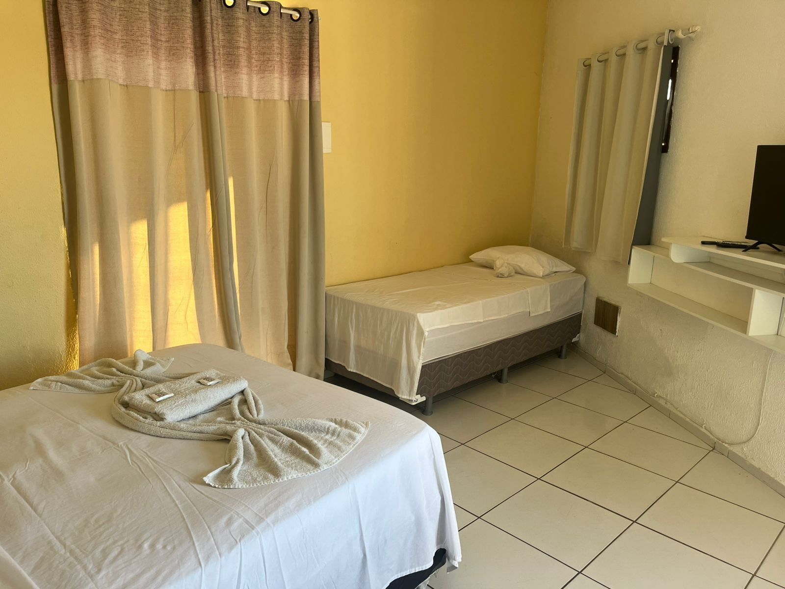 A hotel room with two beds, a TV on a shelf, and a bathroom with a shower curtain.