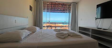A hotel room with a bed, a TV, a balcony with a view of the beach, and a ceiling fan.