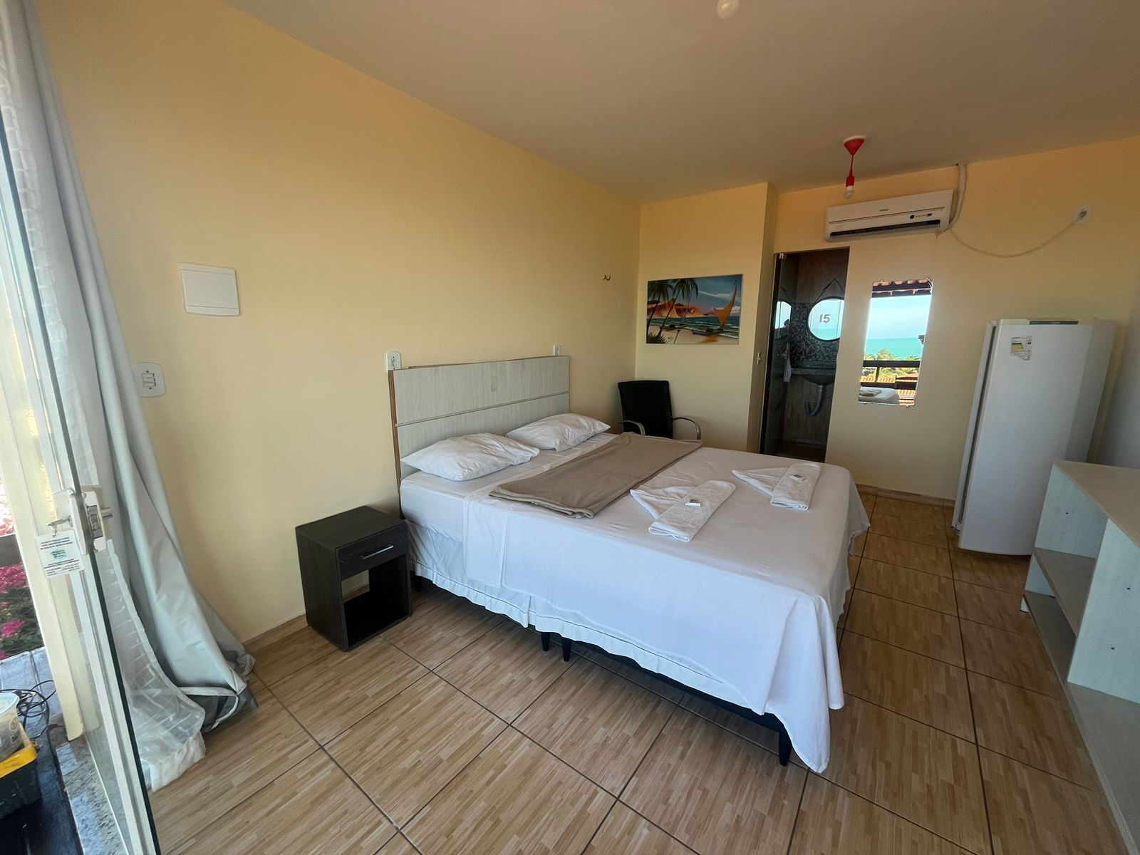A hotel room with a bed, a small bedside table, a wardrobe, and an air conditioning unit.