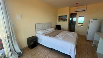 A hotel room with a bed, a small bedside table, a wardrobe, and an air conditioning unit.