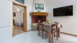 A dining area with a table set for two, a television mounted on the wall, and a fireplace with a vase on the mantle. - 3342 Casa di Enza by Barbarhouse (Ugento)