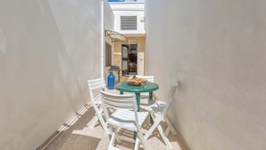 A narrow outdoor patio with a round table and white chairs, a blue gas cylinder, and a small grill. - 3342 Casa di Enza by Barbarhouse (Ugento)