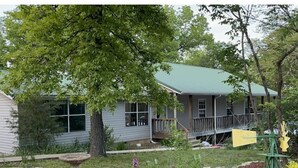 A single-story house with a green roof, a front porch, and a small deck. - HOT TUB - The Lodge - 4 bedroom home at Table Rock Lake - 2 blocks from water (Eagle Rock)