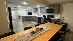 A modern kitchen with grey cabinets, a black microwave, and a wooden dining table with a placemat and a bowl of nuts. - HOT TUB - The Lodge - 4 bedroom home at Table Rock Lake - 2 blocks from water (Eagle Rock)