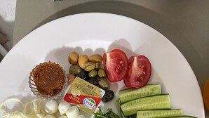 Een bord met diverse soorten eten, zoals tomaten, komkommers, kaas, olijven en kruiden.