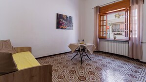 A room with a patterned floor, a wooden sofa with yellow cushions, a small table with a white tablecloth, and a window with curtains. - 3459 Casetta Mulino by Barbarhouse (Nardò)