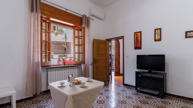A room with a table set for two, a television, and a window with curtains. - 3459 Casetta Mulino by Barbarhouse (Nardò)