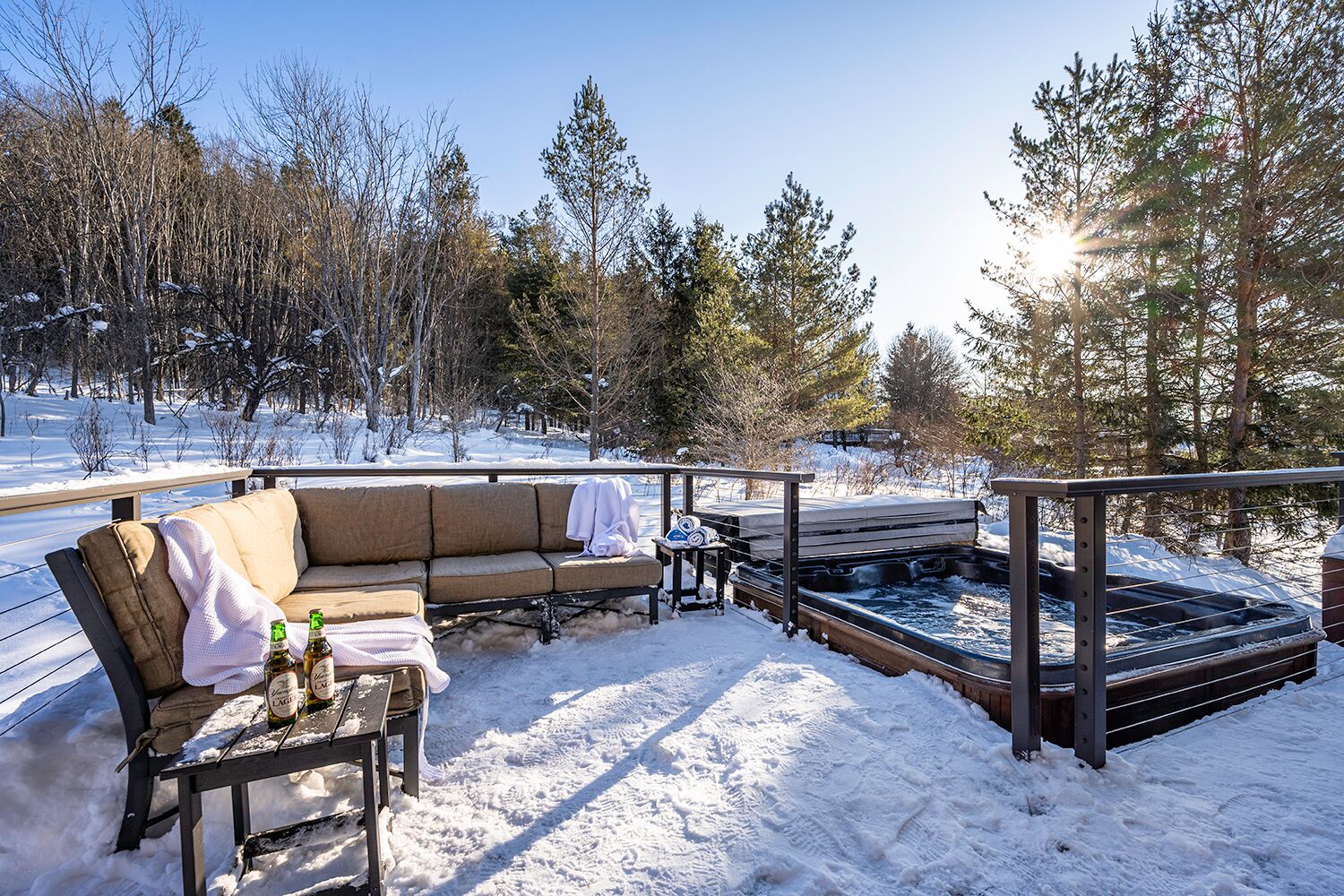 Un espacio exterior cubierto de nieve con un sofá, una mesa con botellas y un jacuzzi.