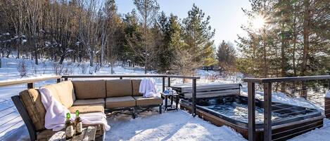 Un espacio exterior cubierto de nieve con un sofá, una mesa con botellas y un jacuzzi.