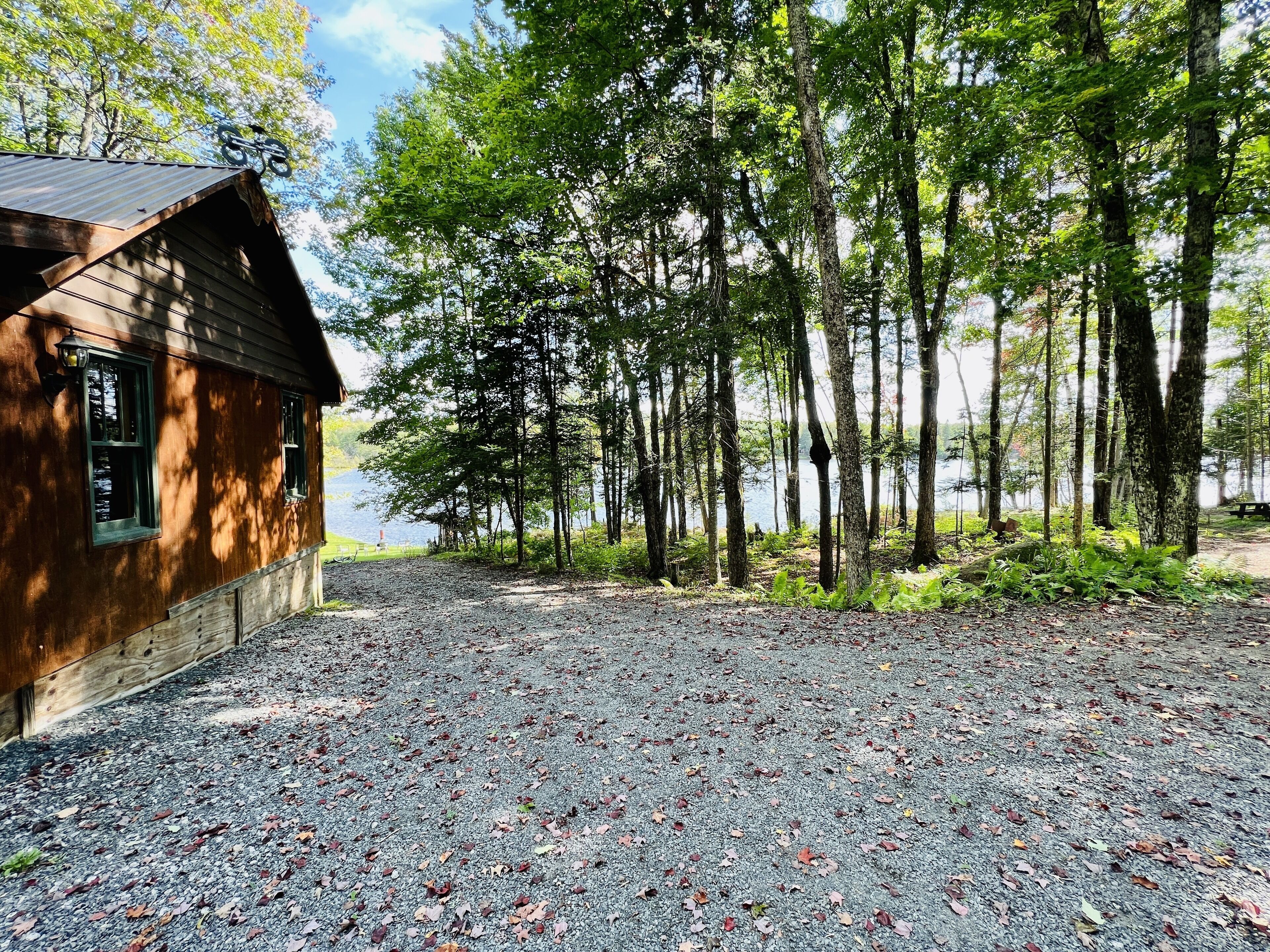 A rustic cabin with a gravel driveway and a forested area in the background.