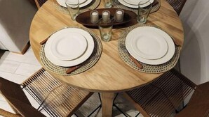 A round wooden dining table with four chairs, each with a woven seat and backrest. The table is set with white plates, cutlery, and glasses.