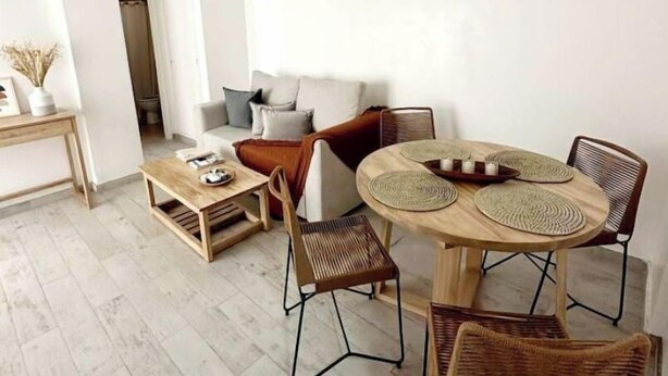 A modern living room with a round wooden dining table, wicker chairs, a sofa, and a coffee table.