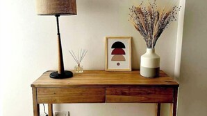 A wooden desk with a lamp, a vase with dried flowers, and a framed picture.