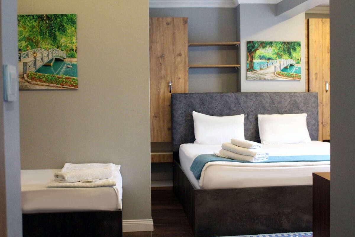 A hotel room with a bed, a nightstand, a wooden wardrobe, and two paintings of a bridge over a river.
