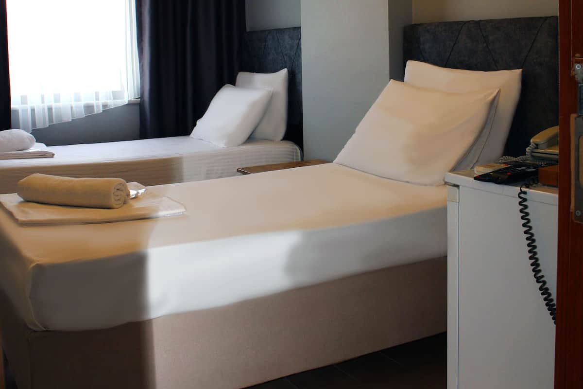 A hotel room with two beds, a small desk, a telephone, and a window with curtains.