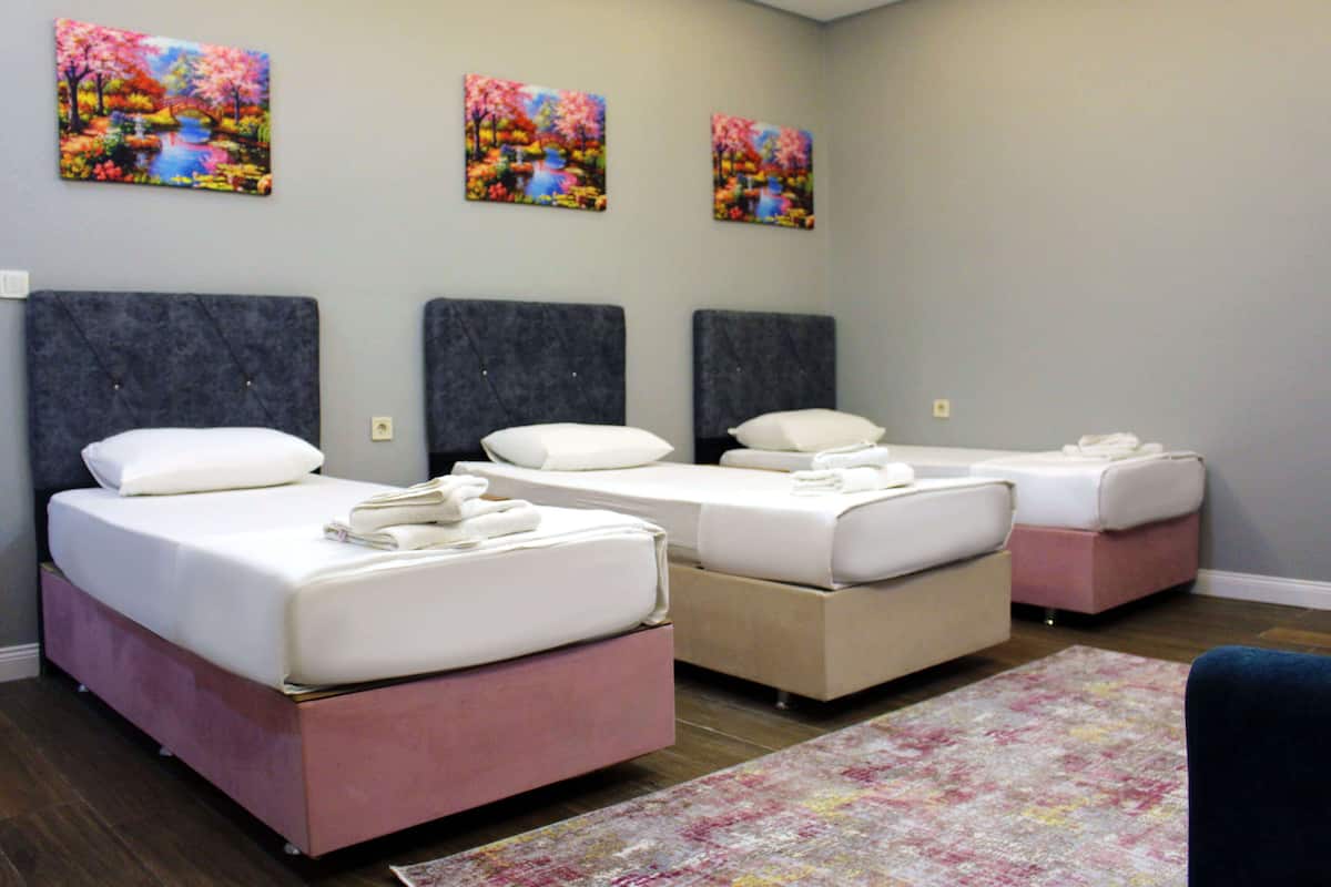 A hotel room with three beds, each with a headboard and white bedding. There are three paintings on the wall above the beds.