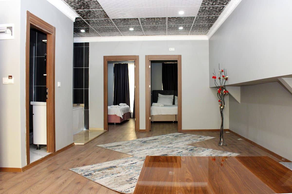 A hotel room with a wooden floor, a large mirror, a bed, a bedside table, and a decorative vase.