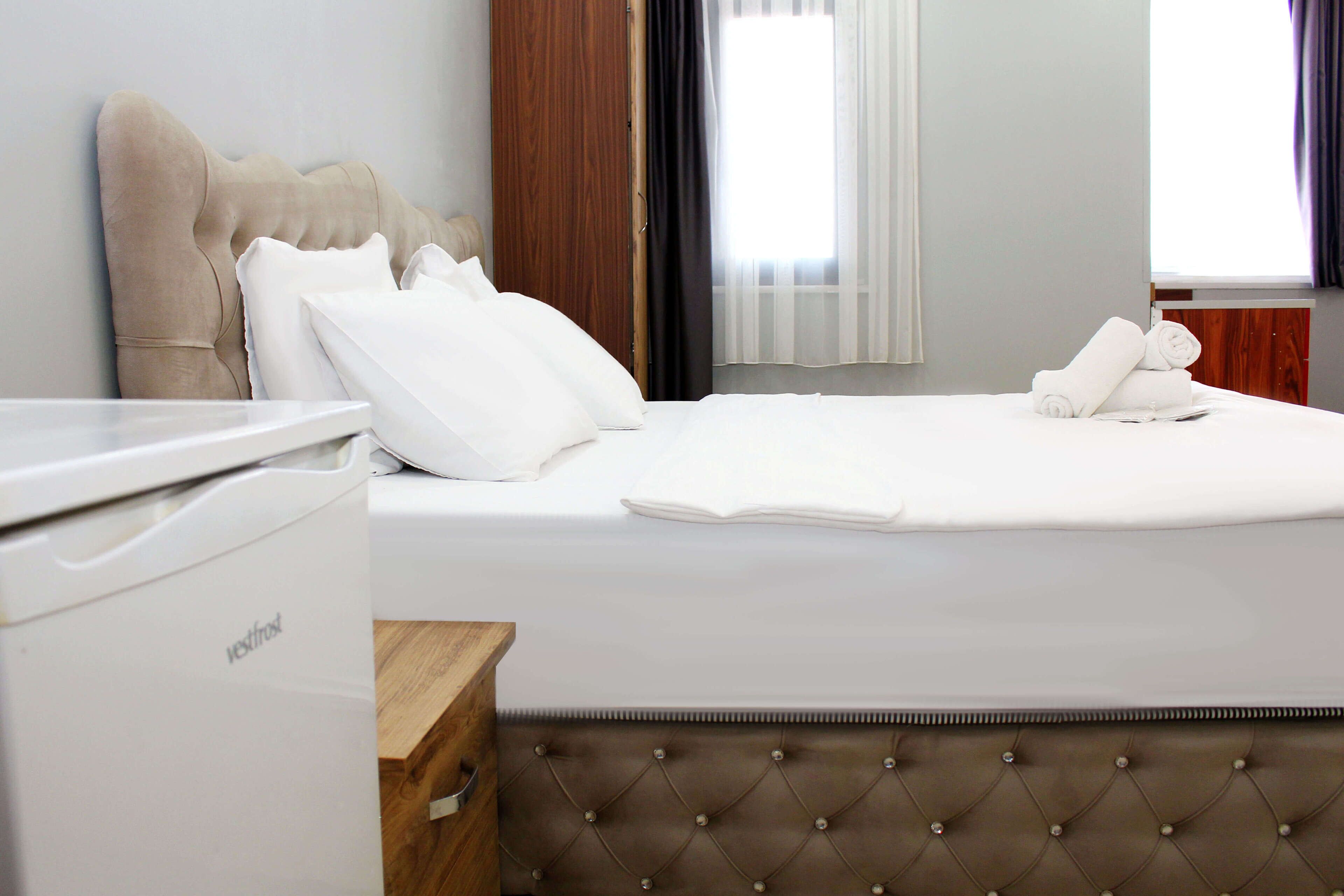 A hotel room with a bed, a wooden dresser, and a white appliance.