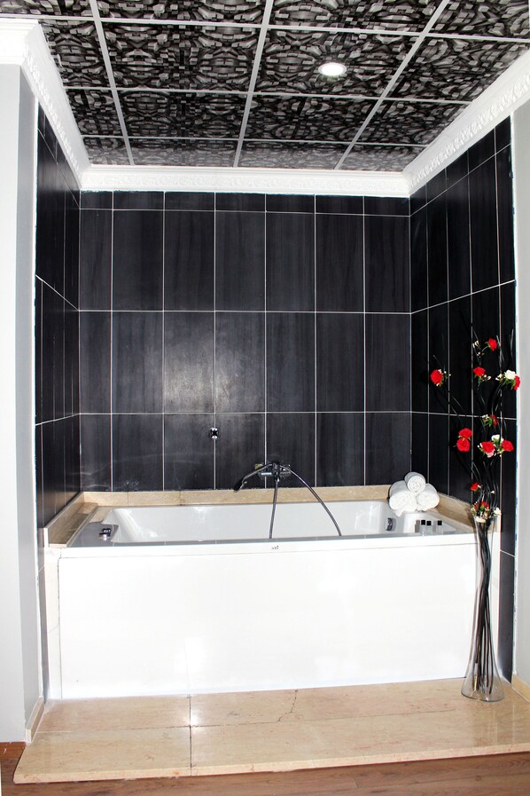 A bathroom with a bathtub, dark tiled walls, and a decorative ceiling.