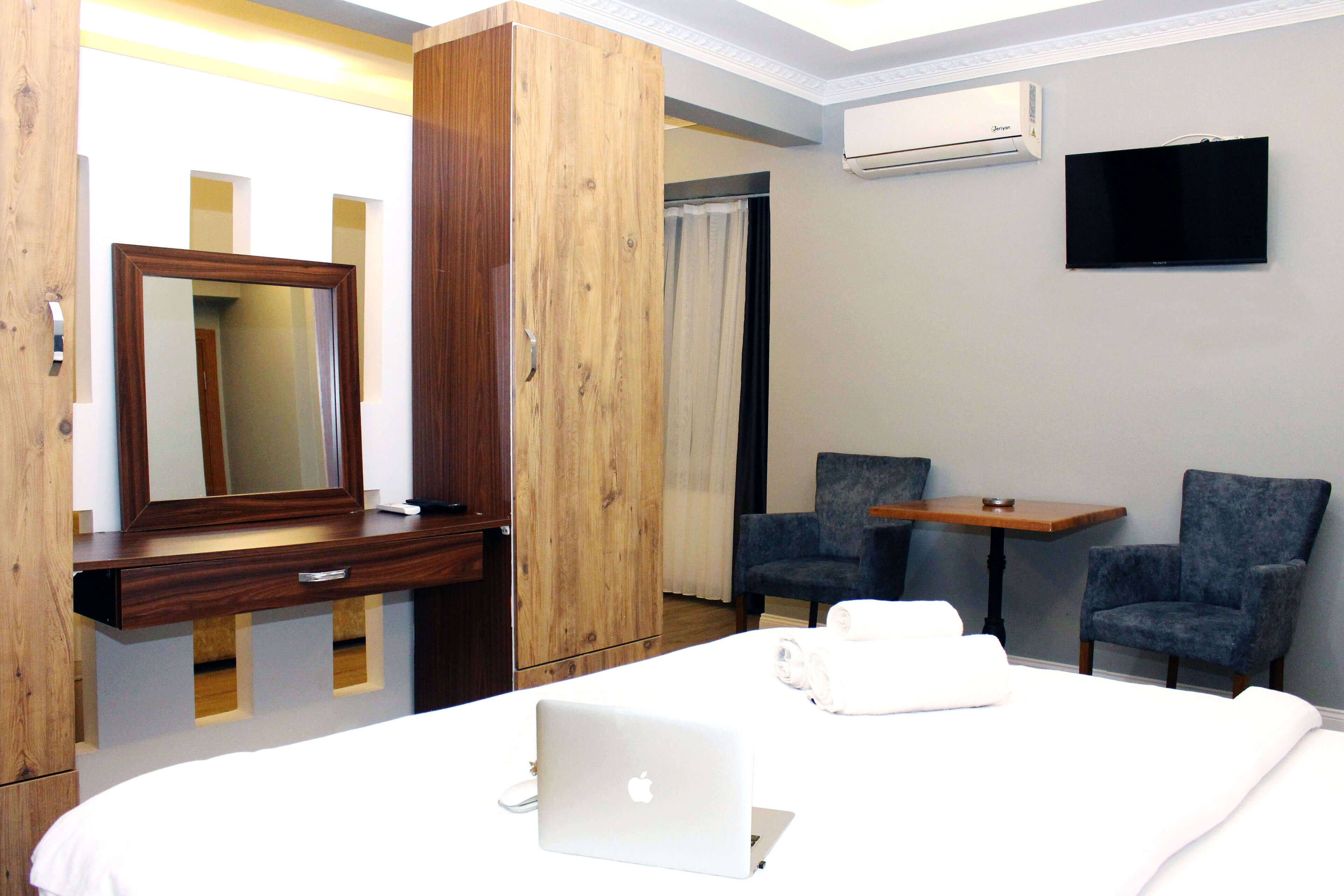 A hotel room with a bed, a desk, a chair, a TV, and an air conditioning unit.
