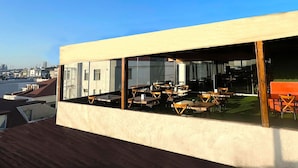 Una terraza en la azotea con mesas y sillas, ventanas amplias y vistas al horizonte de la ciudad.