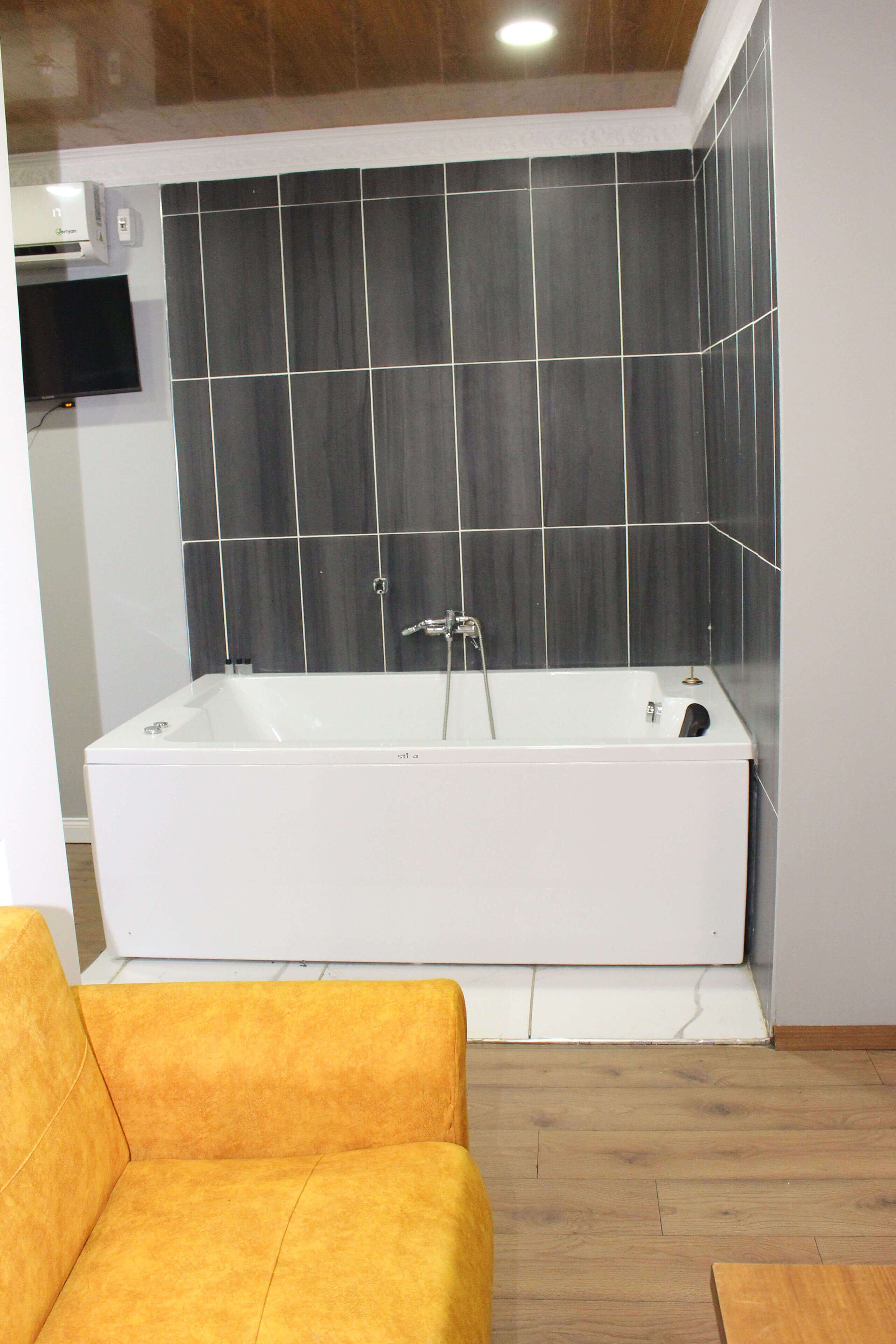 Un baño moderno con una bañera grande, piso de madera y televisor montado en la pared.
