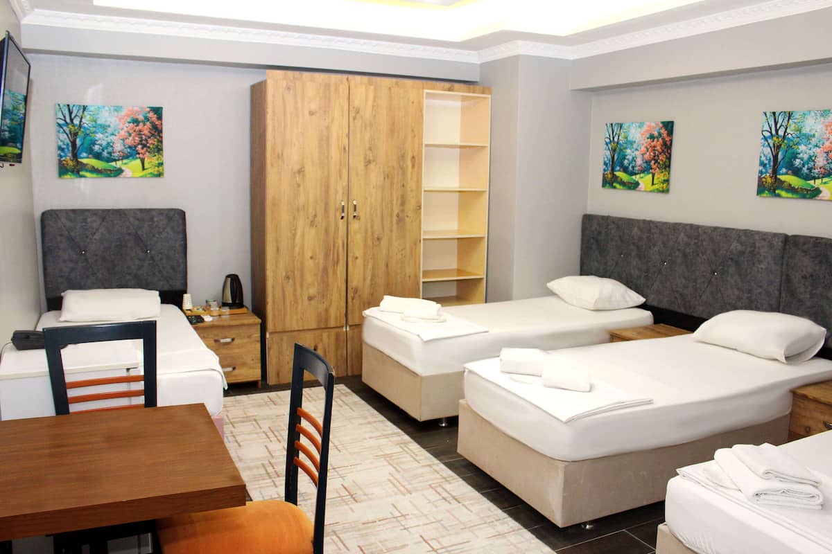 A hotel room with two single beds, a wooden wardrobe, a desk with a chair, and a small table.