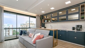 A modern living room with a grey sofa, a wooden coffee table, and a view of the city through large windows. - WI-FI 500MB | Sea View Studio with Foodhall #CA47 (Florianópolis)