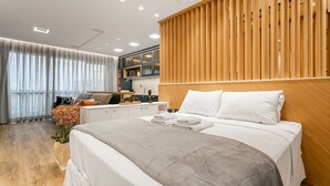 A modern hotel room with a large bed, wooden panel wall, and a view of the city through large windows. - WI-FI 500MB | Sea View Studio with Foodhall #CA47 (Florianópolis)