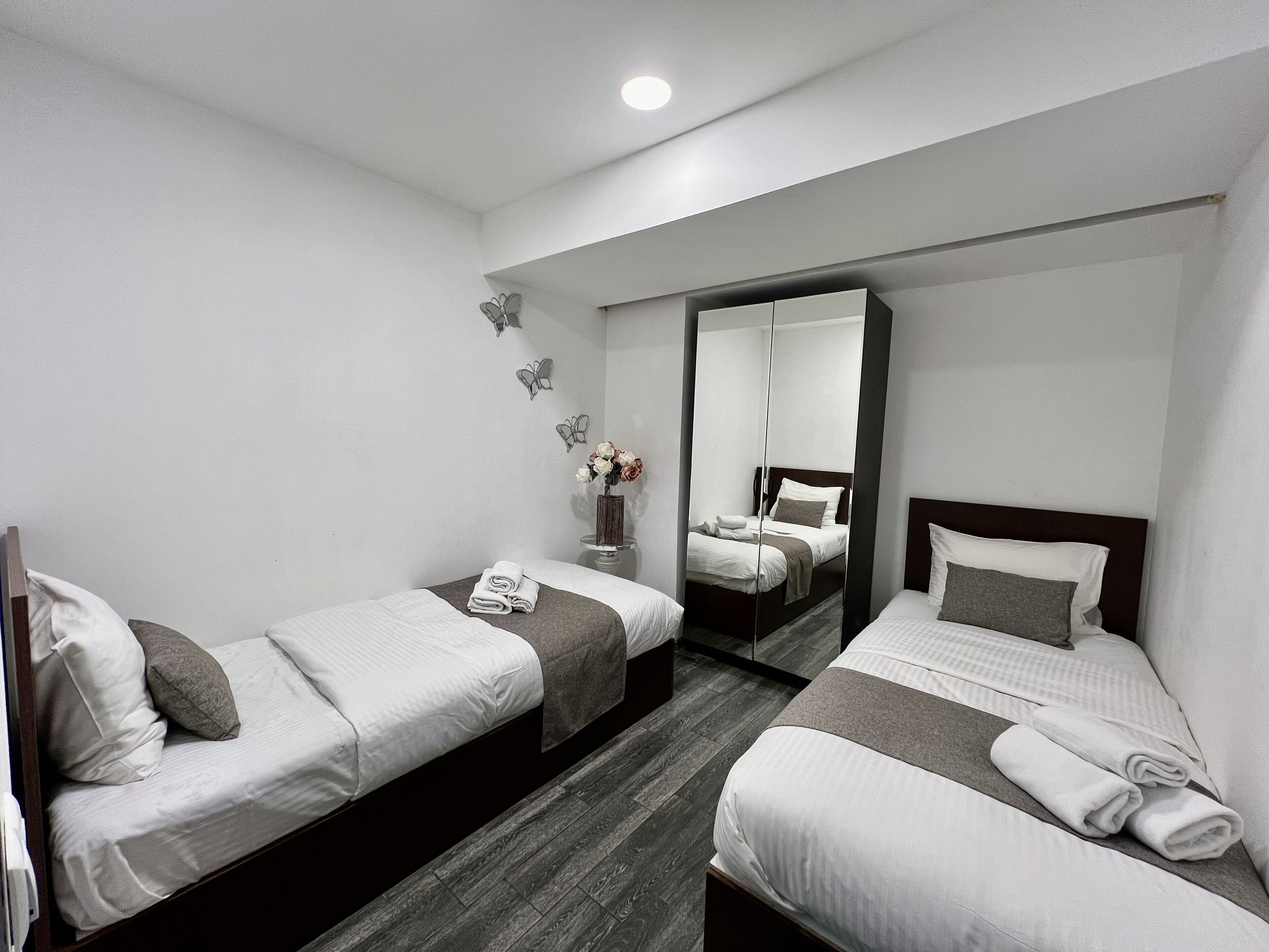 A hotel room with two single beds, a mirror, and a small table with a vase of flowers.