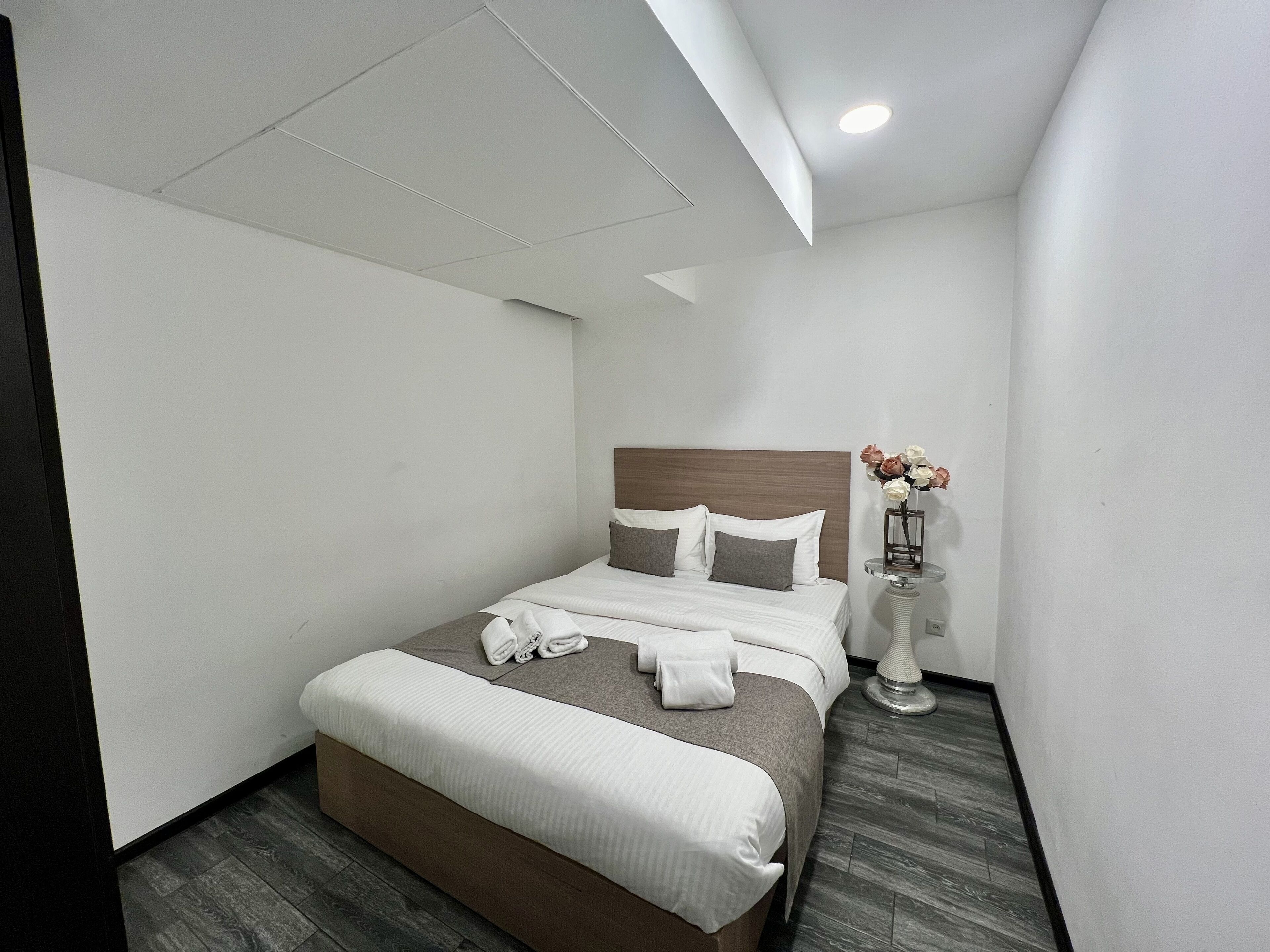 Una habitación de hotel moderna con una cama bien hecha, una mesita de noche con un florero y una pequeña mesa redonda.