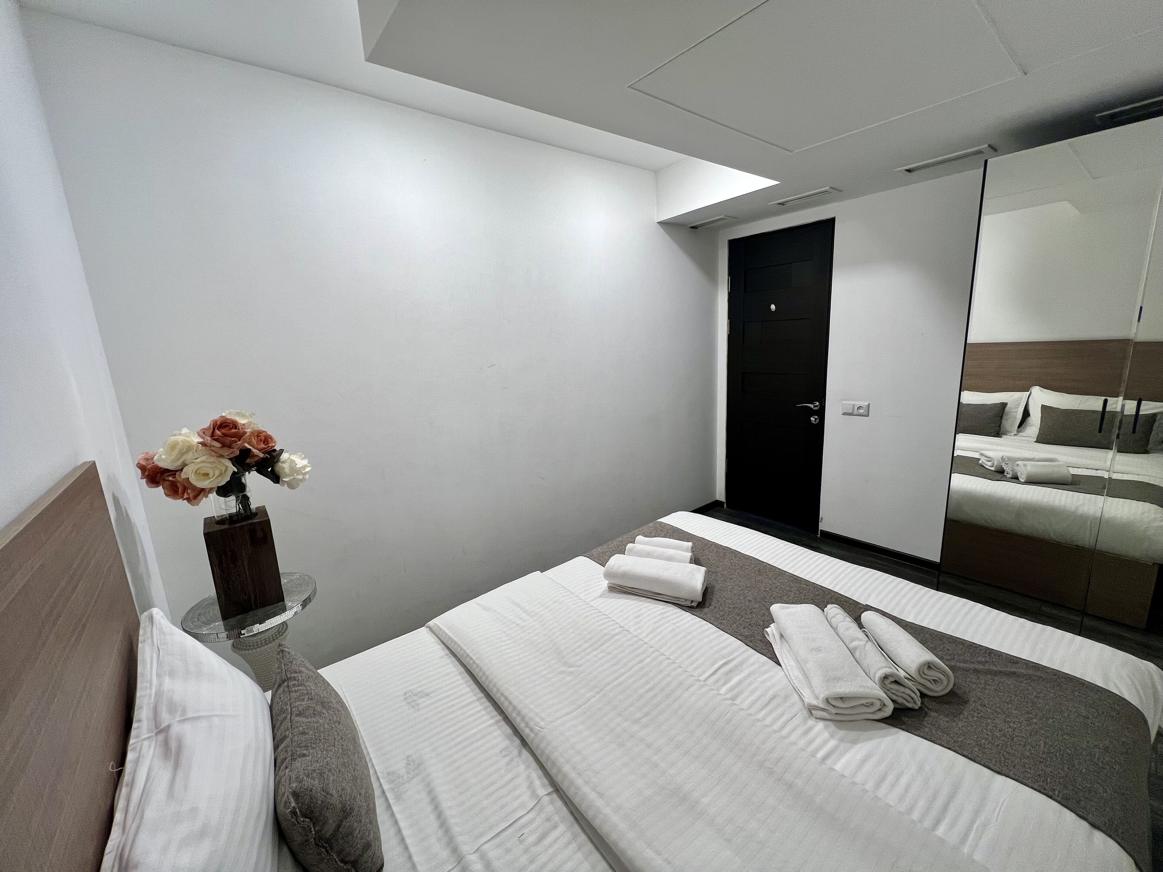 Una habitación de hotel con una cama bien hecha, un florero y un espejo grande que refleja la cama y una puerta.