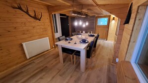 Un intérieur en bois avec une table à manger dressée pour quatre personnes, un radiateur et une grande fenêtre.