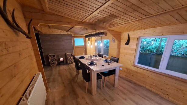 Une cabane en bois comprenant un coin repas, une cheminée et une fenêtre donnant sur un paysage verdoyant.