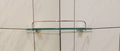 Un baño con baldosas de mármol blanco y dos estantes de vidrio fijos a la pared.