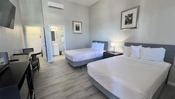 A hotel room with two beds, a desk, and a bathroom visible through an open door.