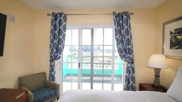 Una habitación de hotel con una cama, una silla, una lámpara y un ventanal con cortinas.