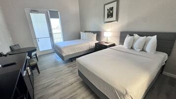 Habitación de hotel con dos camas, un escritorio y una silla. Hay una puerta que da a un balcón.