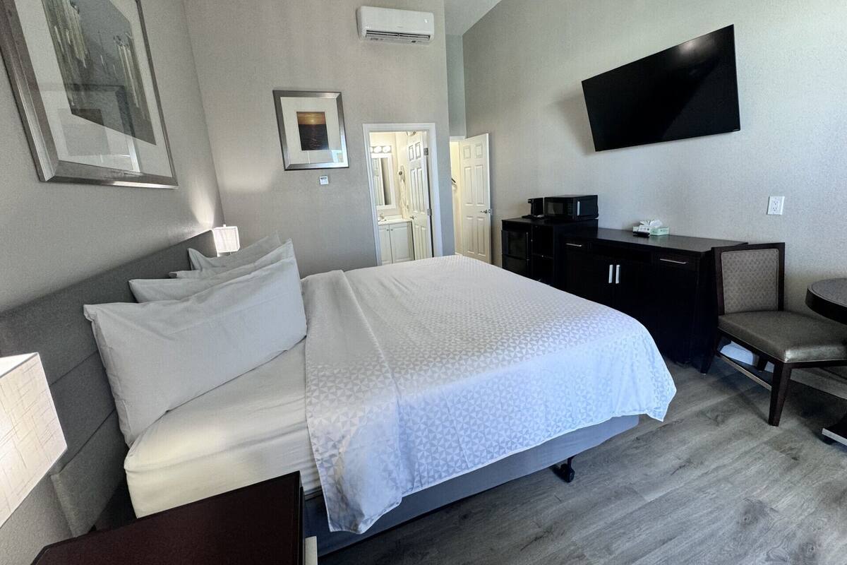 Habitación de hotel con una cama grande, un escritorio con una silla, un televisor de pantalla plana montado en la pared y un microondas sobre el escritorio.