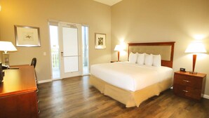 Habitación de hotel con una cama grande, dos mesitas de noche con lámparas, un escritorio con una silla y una puerta que da a un balcón.