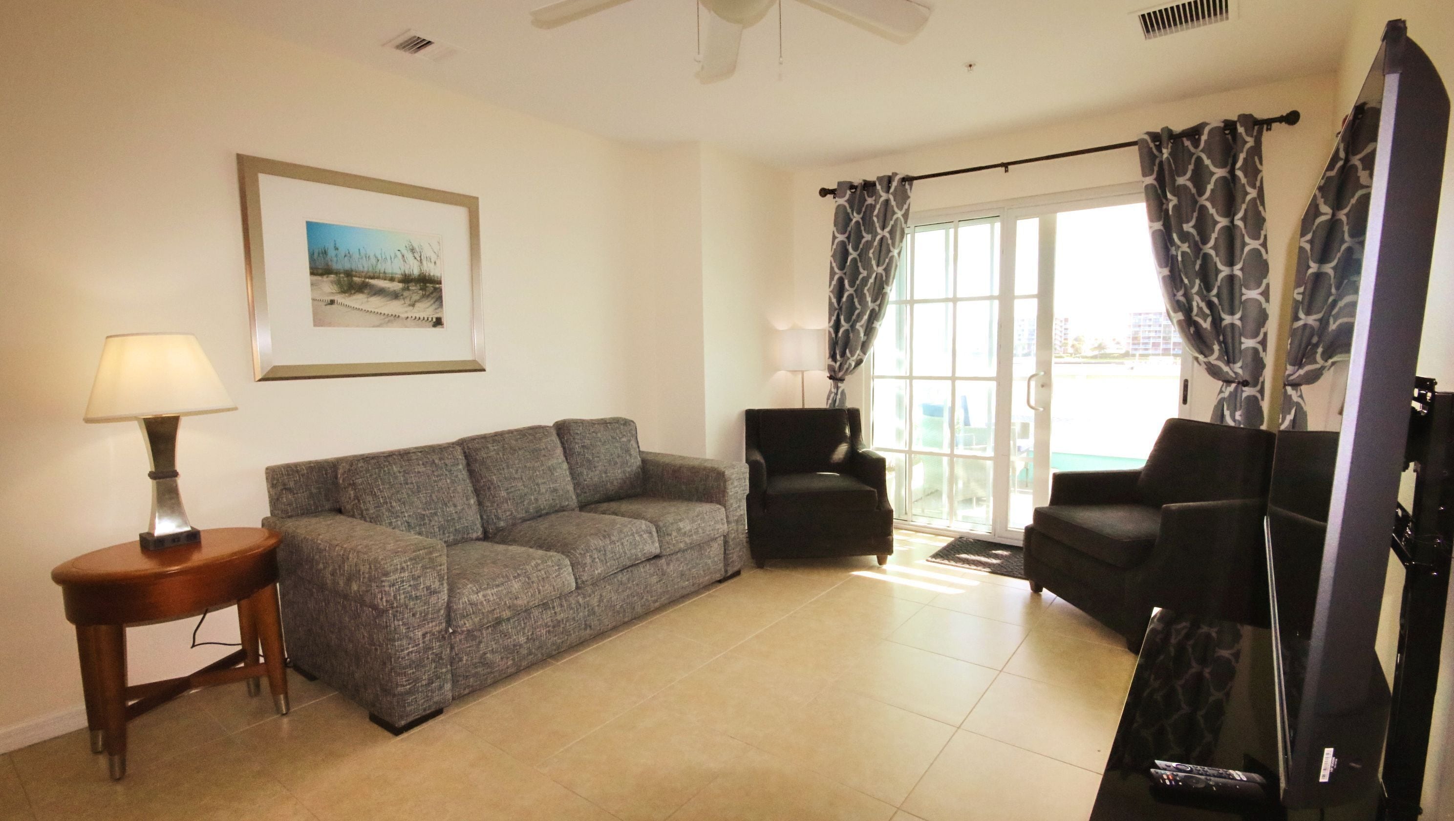 A living room with a sofa, two armchairs, a lamp, and a TV.