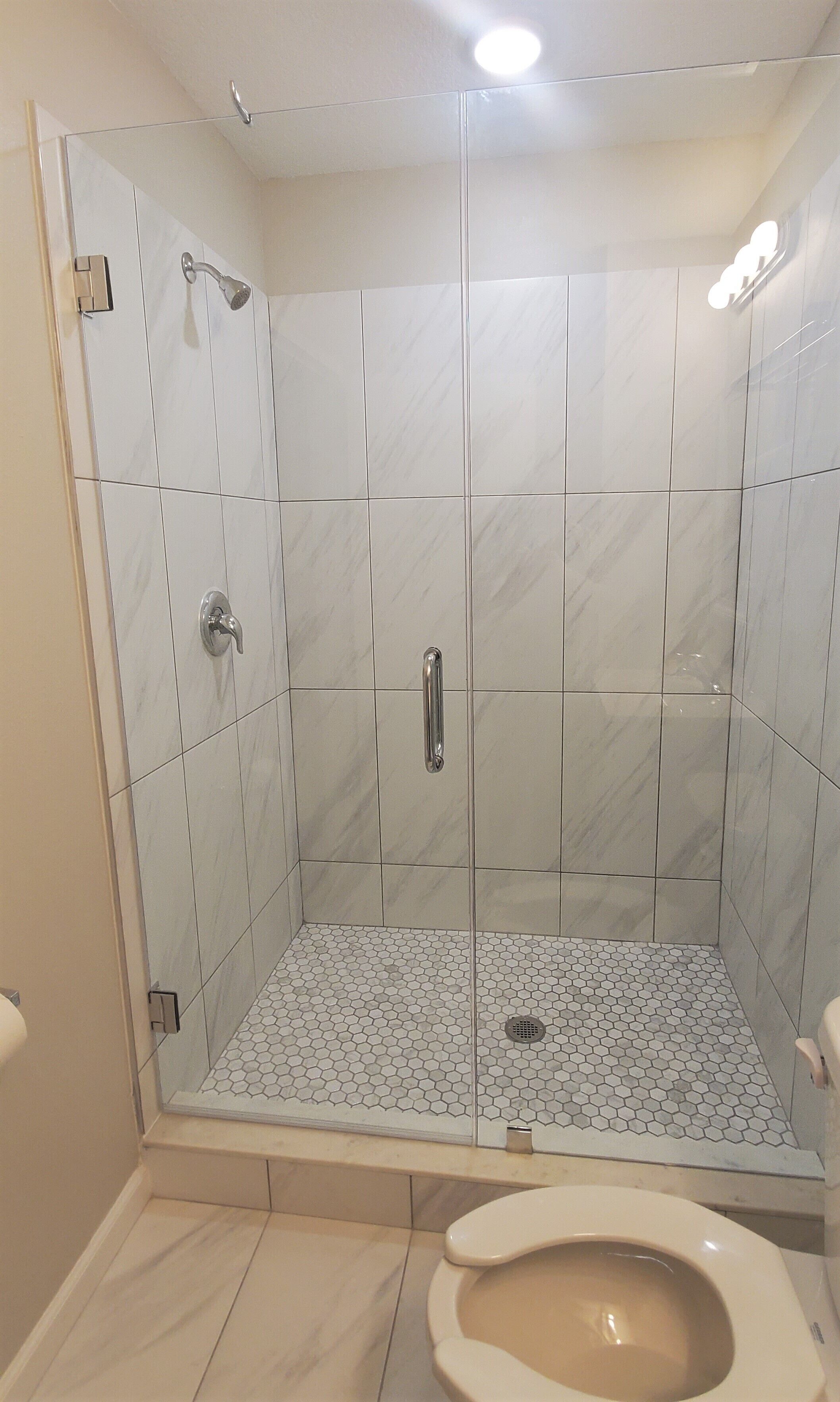 Une salle de bain avec douche, toilettes et carrelage au sol.