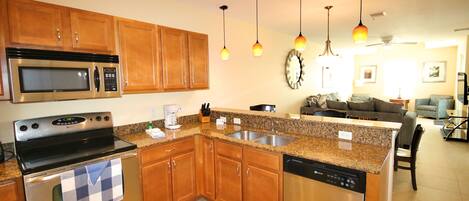 A modern kitchen with granite countertops, stainless steel appliances, wooden cabinets, and pendant lighting.