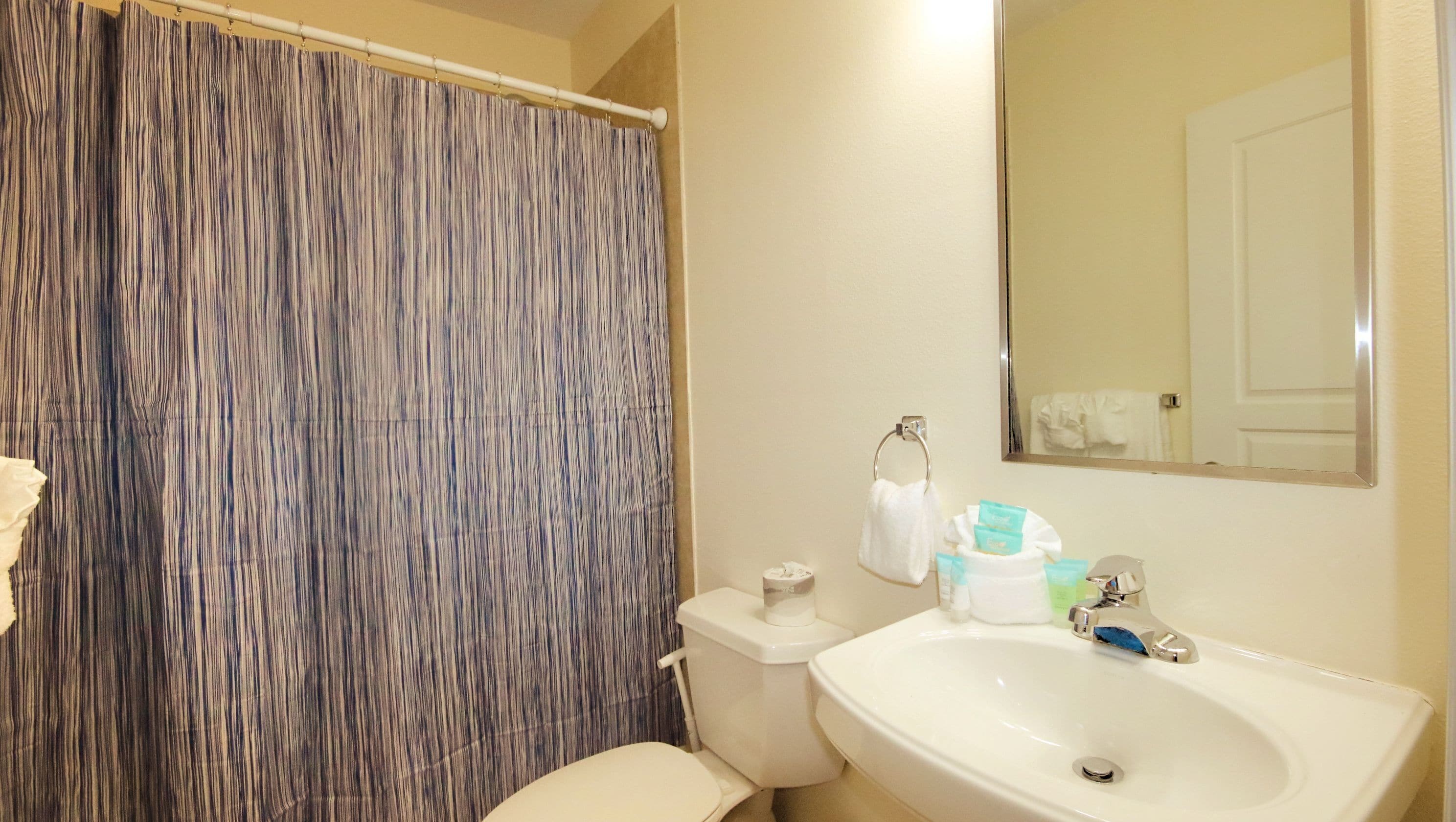 Un bagno con tenda da doccia a righe, un water, un lavandino con articoli da toilette e uno specchio.