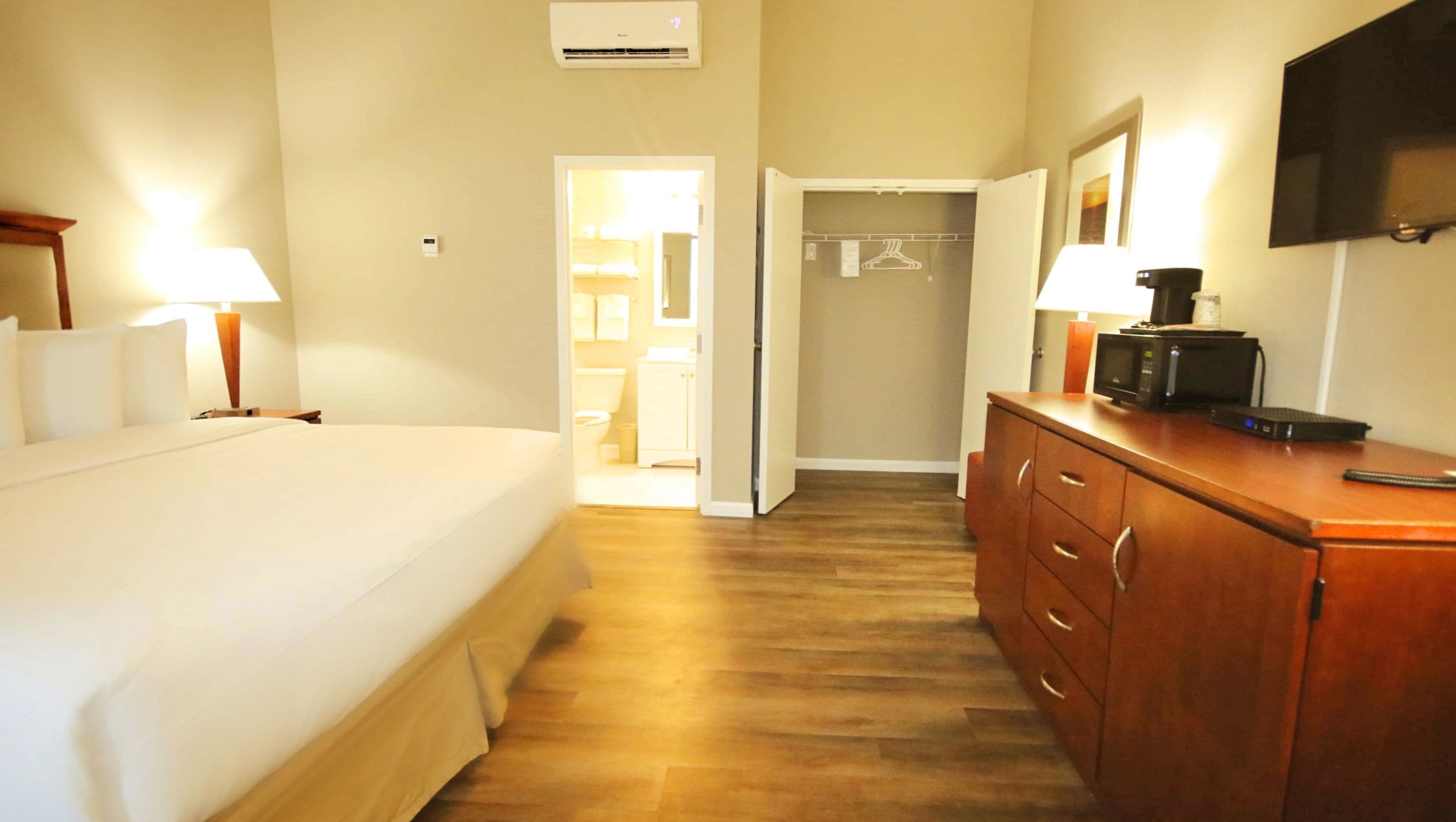 A hotel room with a bed, bedside lamps, a wooden dresser, a flat-screen TV, and a walk-in closet.