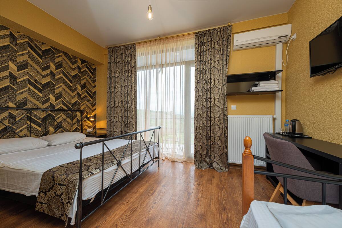 Habitación de hotel con cama, escritorio, silla, televisor y ventana con cortinas.