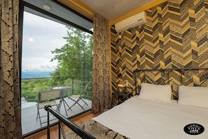 A hotel room with a large window, a bed, a nightstand, and a view of greenery and mountains. - Hotel Villa Lapa (Telavi)